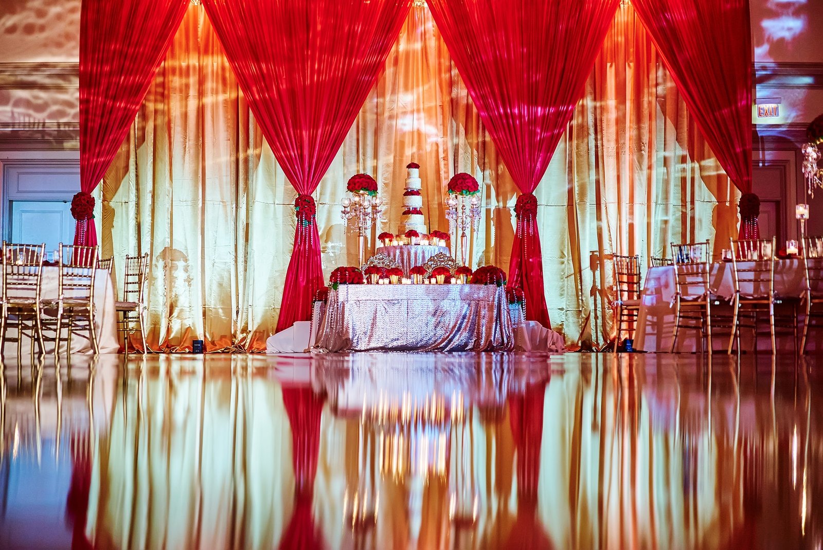 Beautiful reflection of wedding cake and dining table arrangement with gold and red fabric